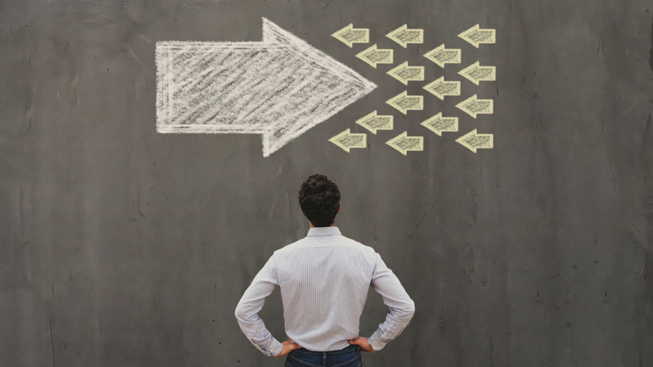 Image of man looking at a chalkboard with drawings of fish swimming into a giant arrow