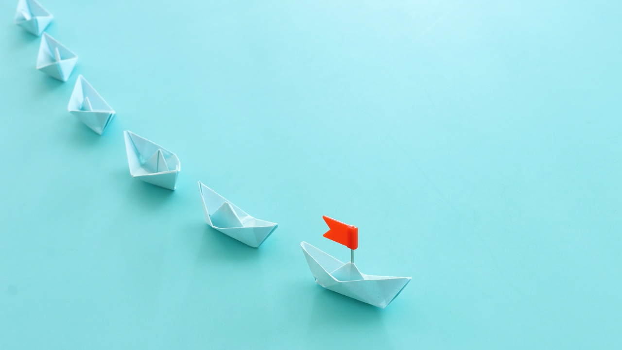 Image of boats being led by a boat with a flag