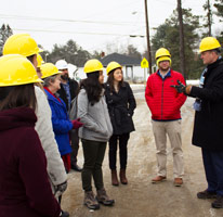 group of college students listening to a developer on the job site and all are wearing yellow hard hats