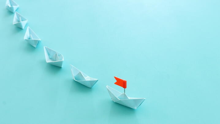 Image of boats being led by a boat with a flag