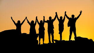 People on top of mountain holding hands up in the air to celebrate a victory