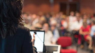 rear view of business woman at lectern lecturing at conference